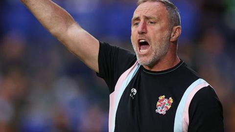 Tranmere manager Andy Crosby raises his right arm arm and shouts from the touchline 