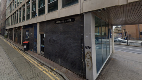 Mulberry Street: a quiet backstreet in central Sheffield. It has dark bricks and concrete windows. There are double yellow lines on the road.