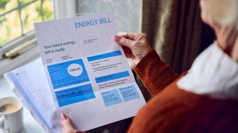 Woman looks at paper energy bill near a window.