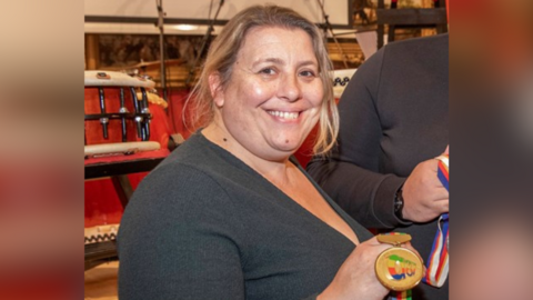 Sarah Russell posing for a publicity photo with a large medal