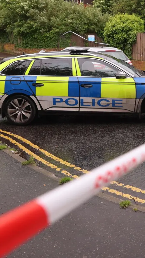 A marked police car is parked behind a red and white cordon.