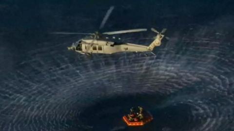 A helicopter awaits to transport a crew member to the recovery ship after being extracted from the Artemis II capsule by recovery personnel in the Pacific Ocean.