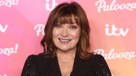 Lorraine Kelly in black sparkle dress in front of a pink branded background covered in logos