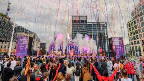 Birmingham Festival 23 opening event, featuring a crowd of people in front of a stage, with streamers pouring down