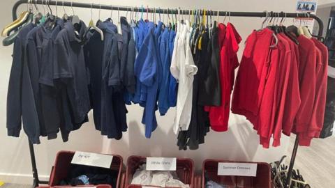 Jumpers and shirts haning from rack with tubs of shirts and PE kit below