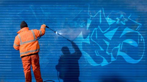 Man in hi vis cleaning graffiti from a roller blind
