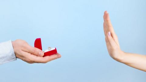 Stock image of a woman holding her hand up in rejection of engagement ring