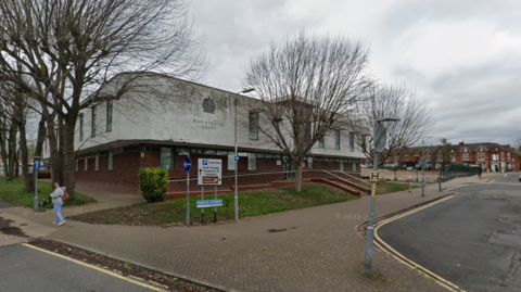 A two storey building with the lower half constructed from red brick and the upper section composed of grey concrete. The upper section also has the words "Magistrates' Court" on the side.