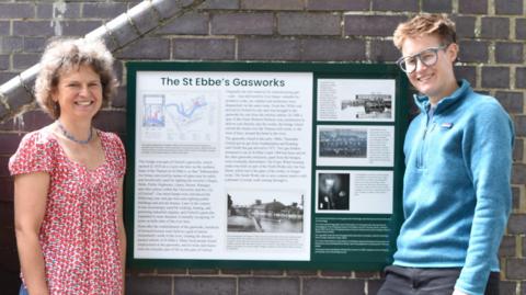 Historian Liz Woolley and councillor Anna Railton posing for a picture on both side of a footbridge history board.