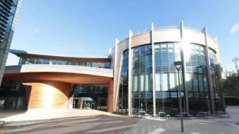 The entrance to one of Durham University's buildings. It is glass fronted with wood panelling. The section to the right is curved.