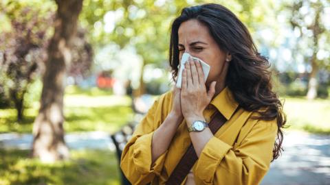 A woman blowing her nose outside.