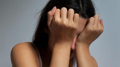 A girl with her head in her hands, rubbing her eyes. She has long dark hair and her face is covered by her hands.