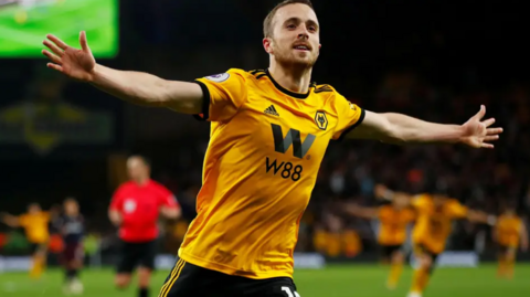 Diogo is in his Wolves kit and on the pitch with his arms outstretched as he runs.