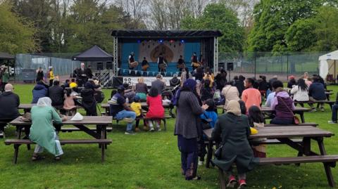 People on picnic benches watching performers on stage at Northampton Eid Festival 2023