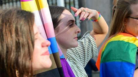 Woman shielding sun from her eyes holding a LGBTQ flag 