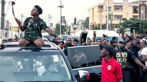 IShowSpeed on top of a car streaming while a crowd watches on
