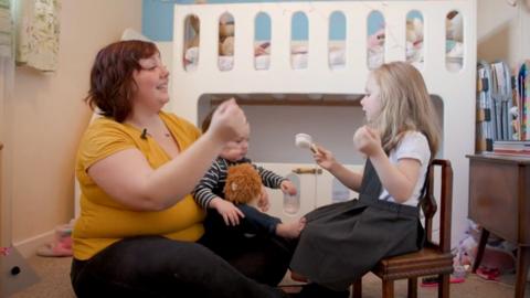 A mum and her two children singing nursery rhymes in a bedroom.