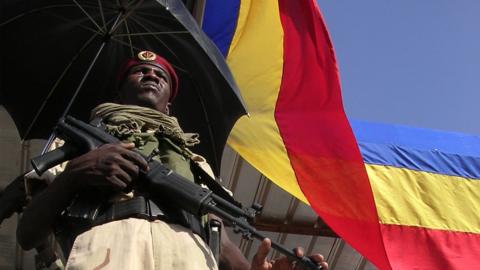 An archive photo of a Chadian soldier holding a gun and standing next to the national flag in 2006.