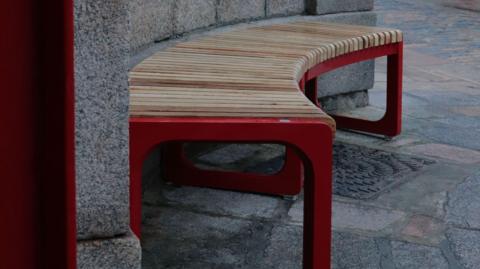 A curved wooden bench, partially painted in red, fits along a curved wall at the market.