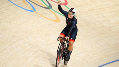 Sophie Capewell, in a dark blue Team GB bodysuit, cycles on a track, celebrating her Paris 2024 Olympics win