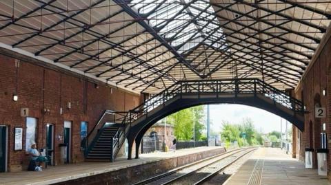 The interior of Filey railway station - a red brick building with two railway tracks running through, and a platform either side. An iron bridge spans the two platforms.