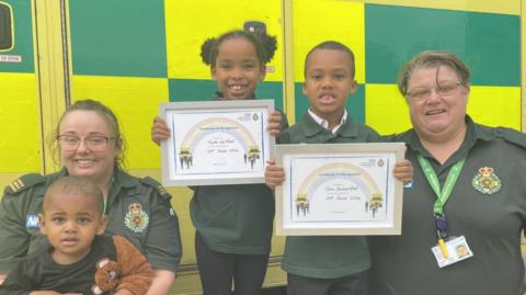 Three siblings smile between two ambulance personnel 