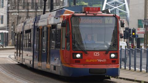 A tram in Sheffield city centre. It is red, orange and blue and displays its destination as 'Middlewood'.