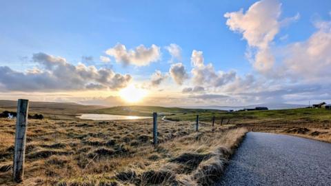 The sun rising over the horizon with blue sky and some clouds and frosty fields in the foreground