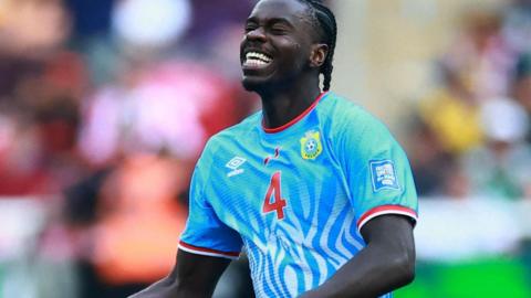 DR Congo defender Axel Tuanzebe celebrates a goal for his country against Jamaica in their World Cup play-off win. He is seen from waist up clenching his right fist at waist level while tilting his head up slightly, with eyes closed and a look of delight on his face