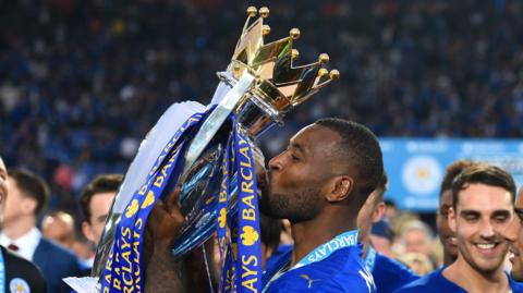 Wes Morgan kisses the Premier League trophy while at Leicester