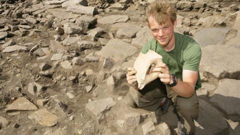 A young man holds a stone relic at Vindolanda