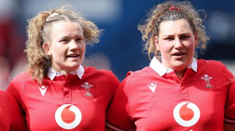 Carys Cox and Gwenllian Pyrs line up for the national anthem ahead of a match