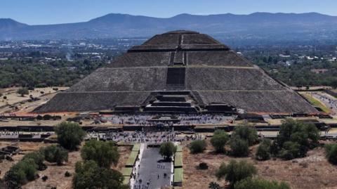 A big pyramid seen from a distance with mountains in the background, and groups of people in the foreground