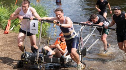 A team struggles through the River Nidd with their bed