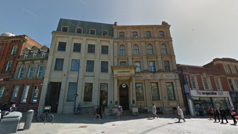 An old-style four-storey building next to a new four-storey building in a high street setting