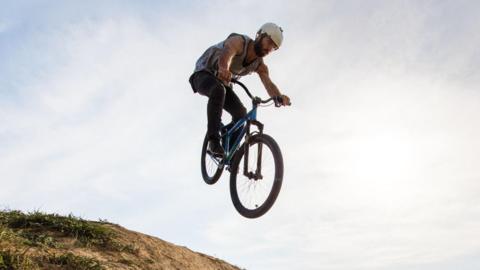 Low angle view of skillful mountain bike rider jumping over dirt hill against the sky. Copy space.