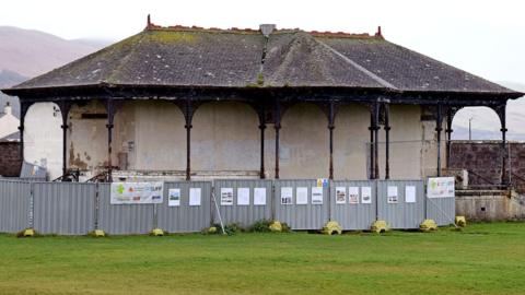 A derelict looking bandstand fenced off in a park