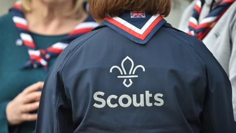 The Scouts logo is seen on the back of an anonymous Scout leader's shirt, with other anonymous Scouts in the background, taken at the Scouts' Headquarters in Gilwell Park, Essex in March 2019.