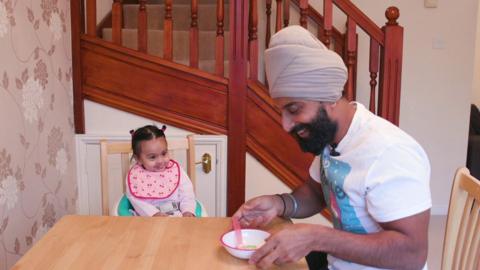 A father and baby daughter have a mealtime at the table while singing a nursery rhyme.