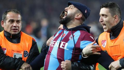 A Trabzonspor supporter is escorted away by security guards