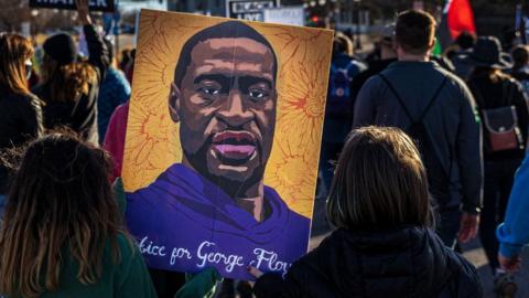 Two kids hold a poster of George Floyd as demonstrators hold signs and flags during the "Justice for George Floyd" march to the Minnesota State Capitol on March 19, 2021 in Saint Paul, Minnesota.