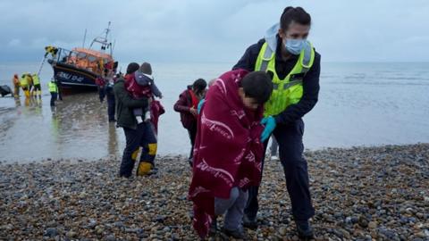 Child migrant being helped up a beach