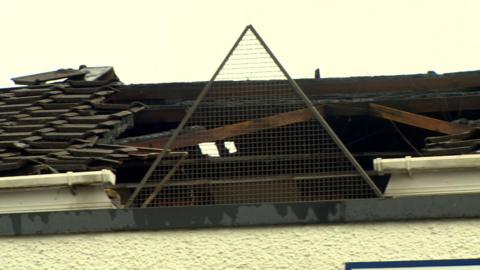 The roof of a building after a fire. Large parts of the roof is missing. The sky is grey and cloudy.