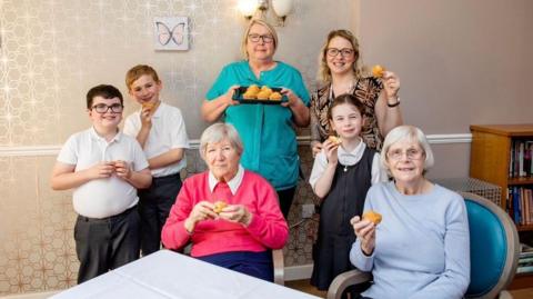 Carers, residents and their families smile as they share cupcakes around a table