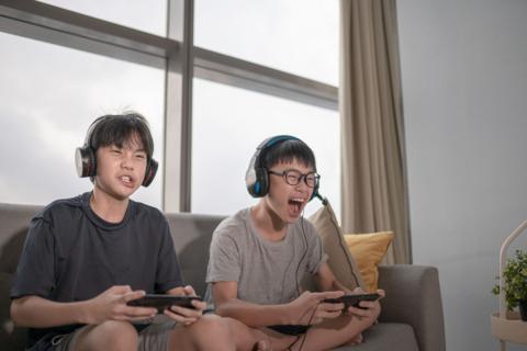 two boys wearing headsets enthusiastically play a video game together