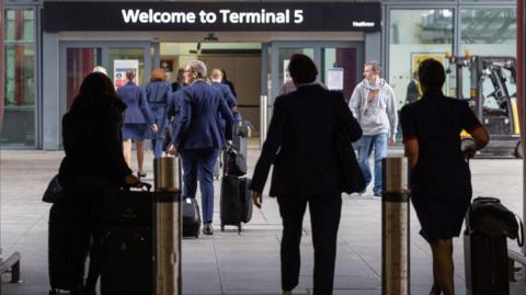 Passengers and airline staff outside Terminal 5 carrying suitcases and other luggage. 