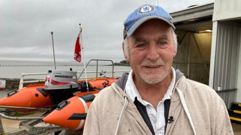 A man wearing a blue Chelsea cap stands outside of an RNLI lifeboat station.