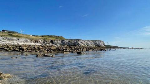 A view of Harrington coastline. Clear, shallow water stretches out before a rocky shore.