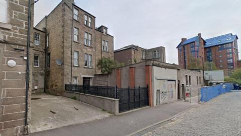 A small car park on a cobbled street, surrounded by tenement flats