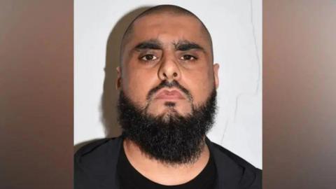 Man with shaven hair and dark beard in black clothing